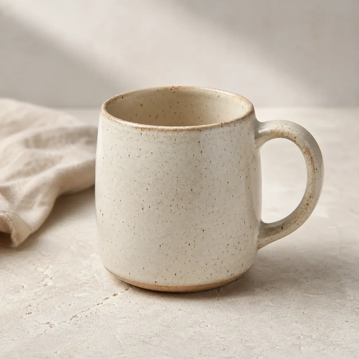 Square ecommerce product image showing a speckled cream ceramic mug on a neutral surface with soft morning light.
